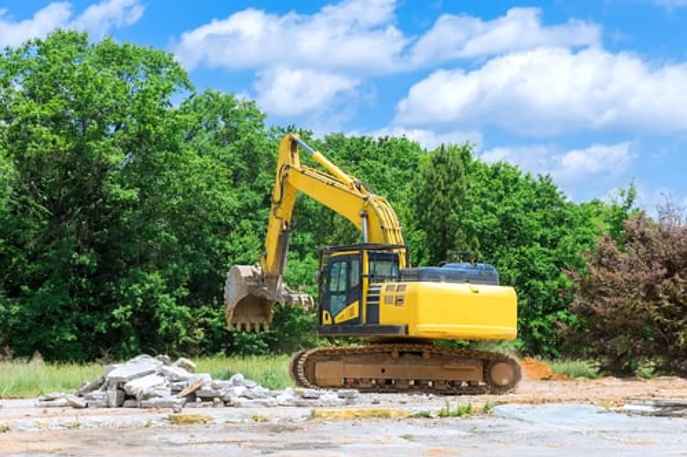 Excavator clearing a residential demolition site under a bright blue sky